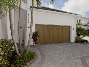 A home with white siding and a paver driveway has a wood garage door.